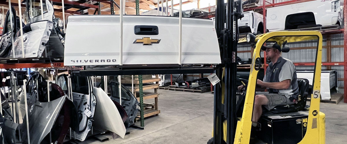 Y Yard tech using a forklift to place a truck tailgate into a parts rack in the warehouse